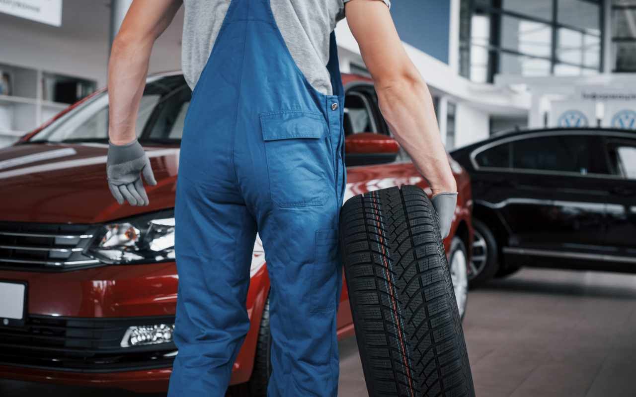 view of a mechanic carrying a winter tyre to a car in a garage