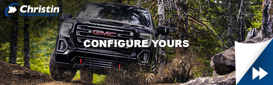 Image of a rugged black configured GMC pickup truck driving down a muddy road in the woods. Image of Christin Chevrolet on the upper left corner