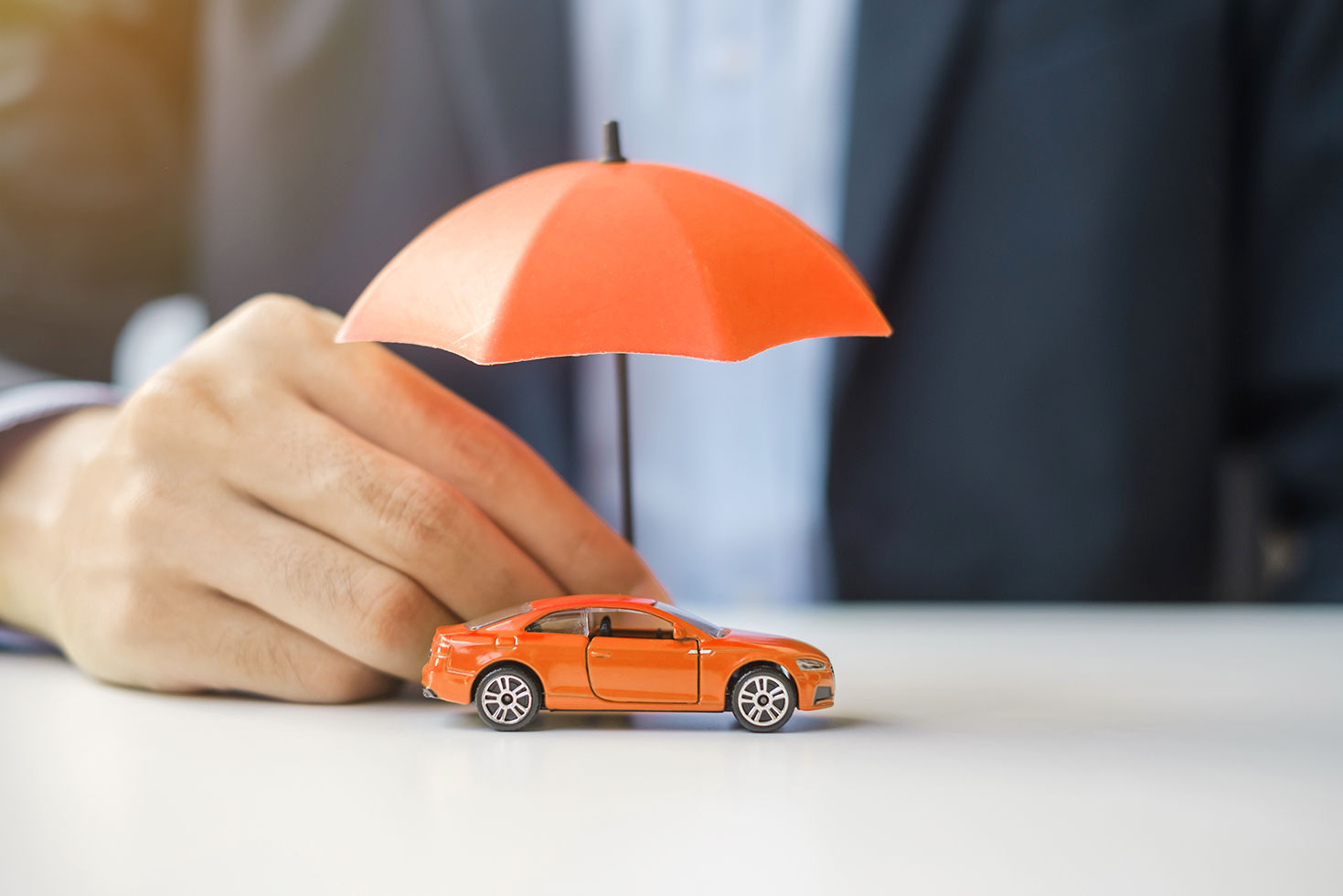 insurance broker holding umbrella above orange toy car 