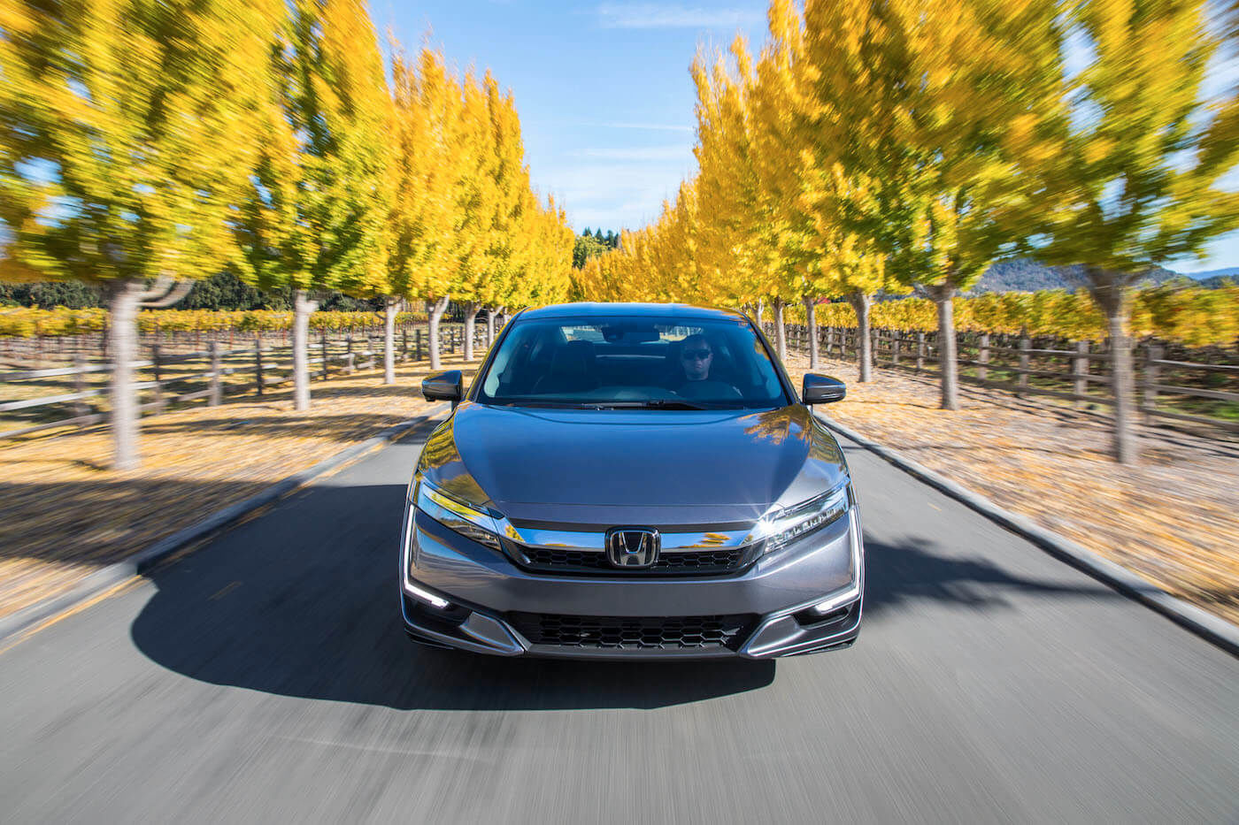 Vue avant de la Honda Clarity hybride rechargeable 2021 grise roulant sur une route longeant les arbres