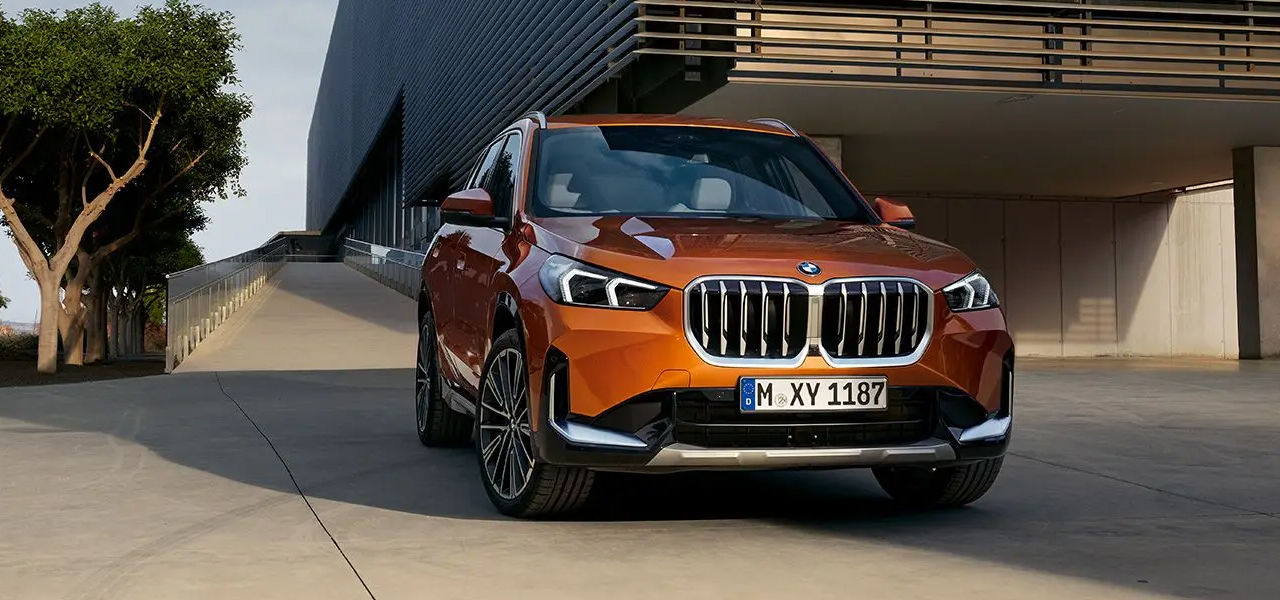 Vue 3/4 avant et latérale du BMW X1 2024 devant un batîment publique, prêt à partir