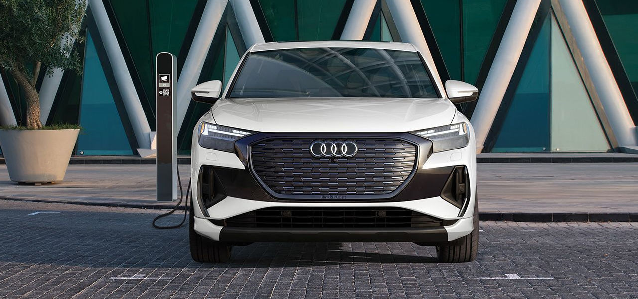 Vue avant de l'Audi Q4 e-tron 2024 avec une borne dans une rue pavé