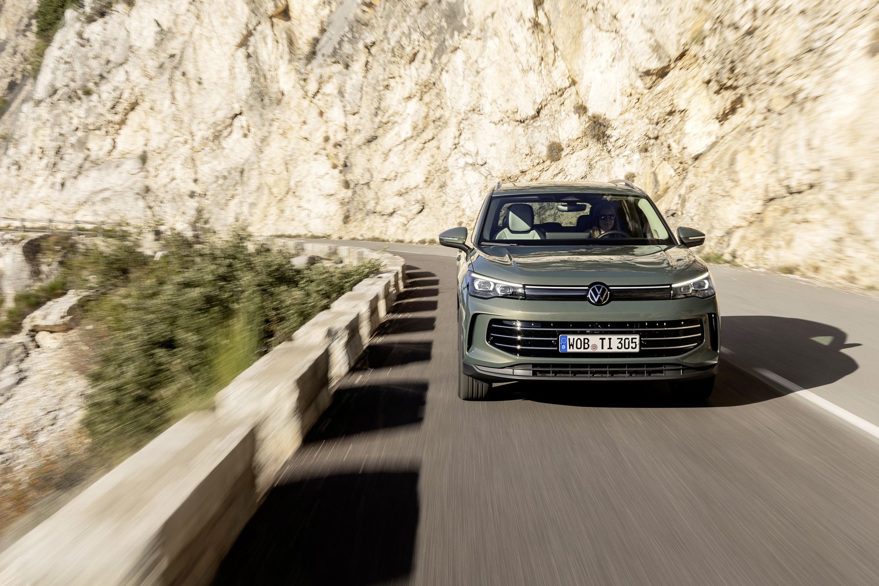 Grey 2025 Volkswagen Tiguan driving through mountain roads with scenic landscape in background.