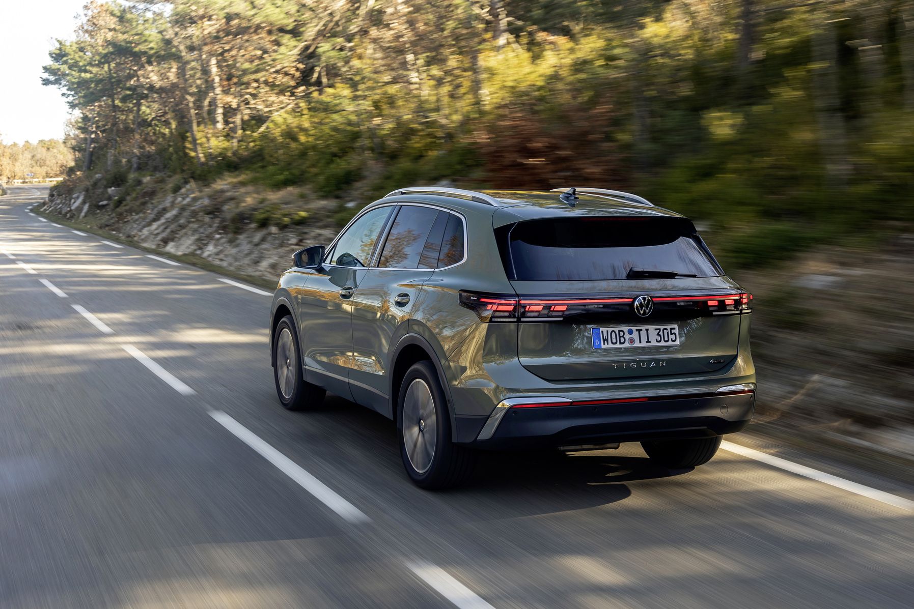 Grey 2025 Volkswagen Tiguan driving on an open scenic highway under clear blue sky.