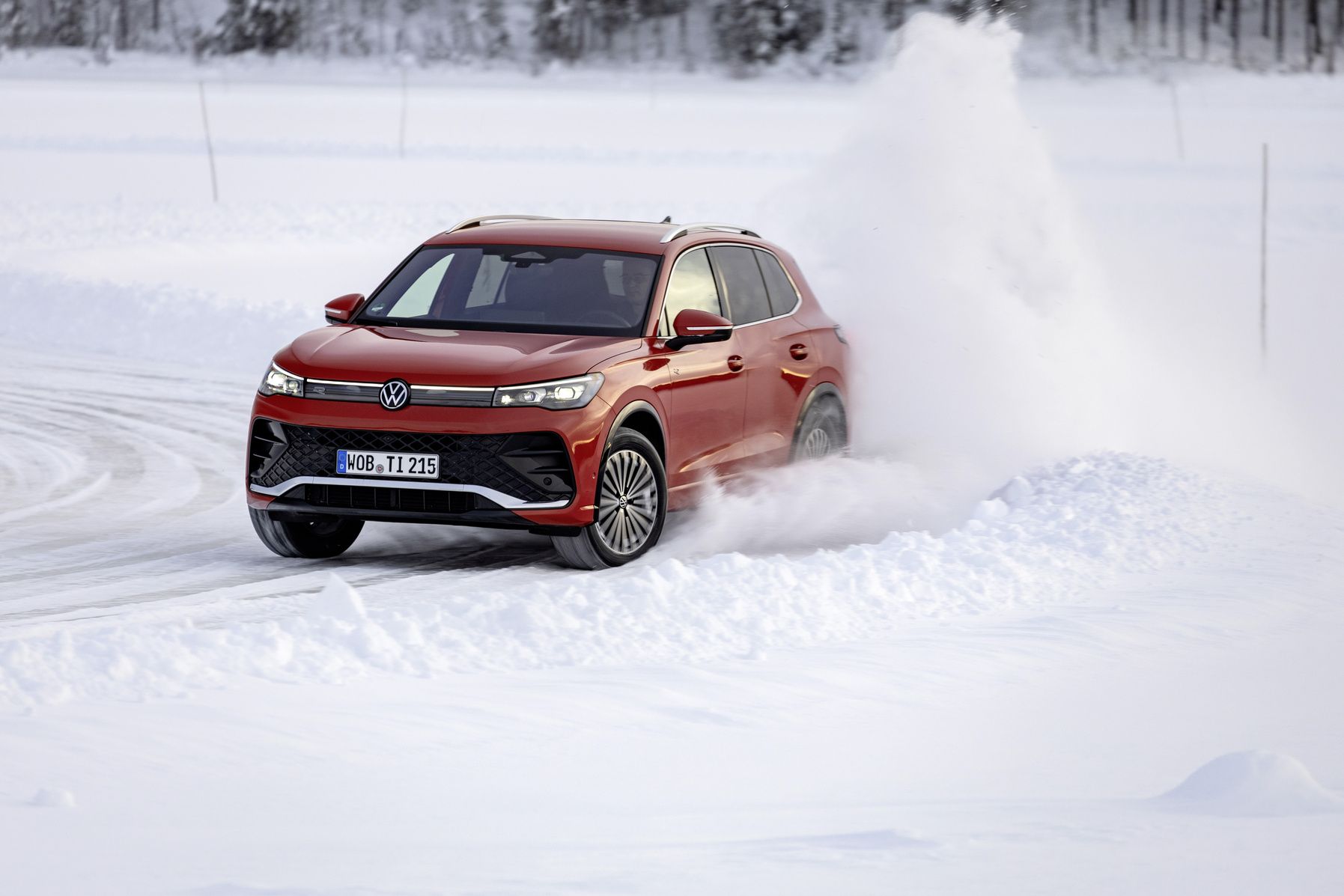 Red 2025 Volkswagen Tiguan parked in snowy environment surrounded by pine trees.