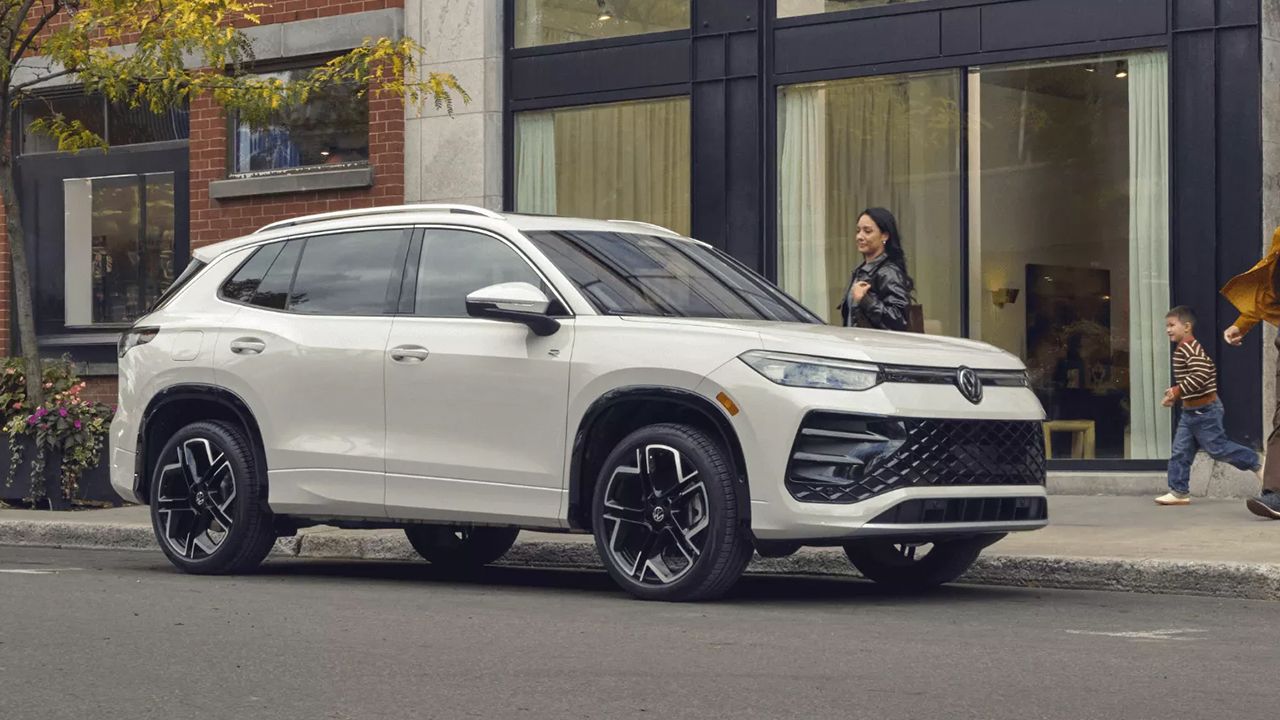 Vue 3/4 avant et lat&eacute;rale de la  Volkswagen Tiguan R-Line&nbsp;4MOTION gar&eacute; en bord de rue, avec famille se dirigeant vers leur nouvelle Volkswagen