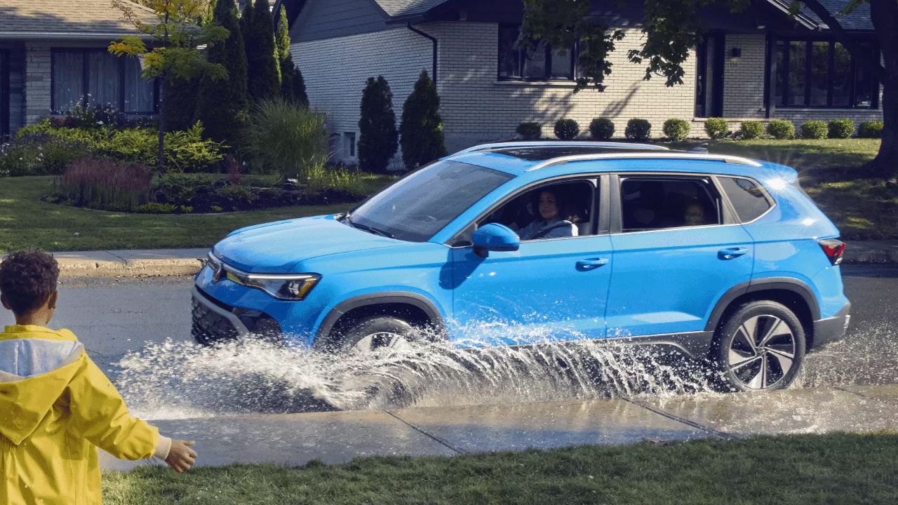 Vue 3/4 avant et lat&eacute;rale de la Volkswagen Taos Comfortline&nbsp;4MOTION traversant une flaque d'eau avec un enfant en imperm&eacute;able