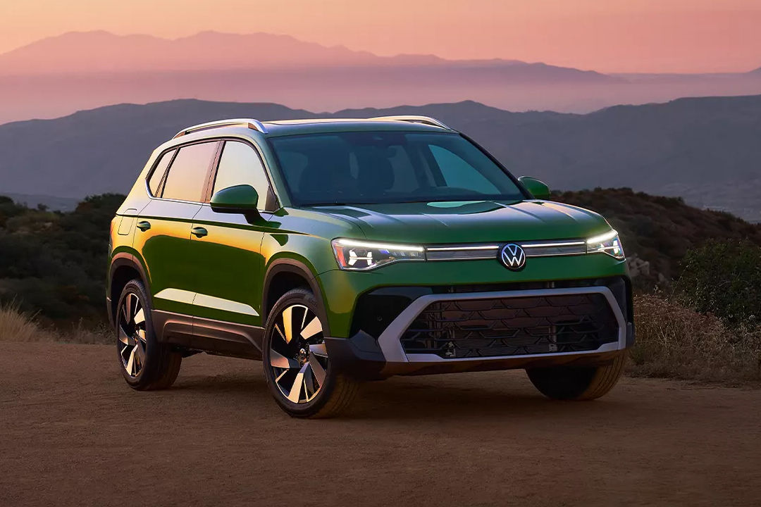 Vue 3/4 avant et latérale du Volkswagen Taos 2025 en arrêt sur la route de sable avec phares allumées et coucher de soleil