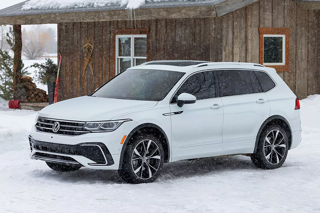 Front and side view of the Volkswagen Tiguan 2024 parked in front of a snow-covered chalet