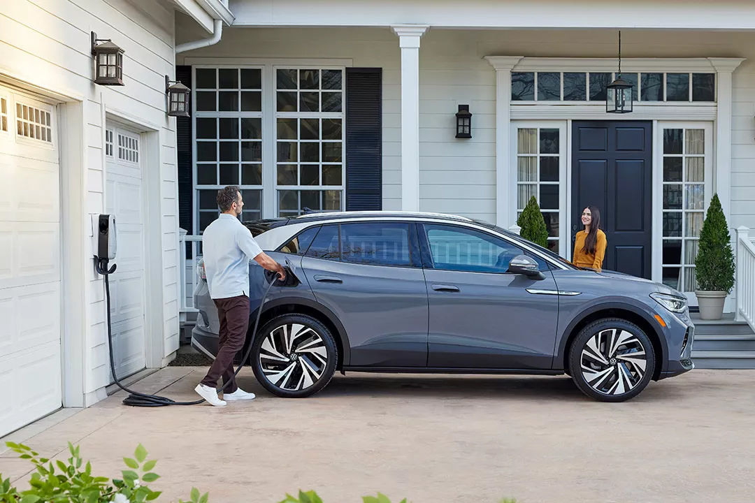 Vue latérale du Volkswagen ID.4 2024 en recharge avec un homme et sa femme à une maison