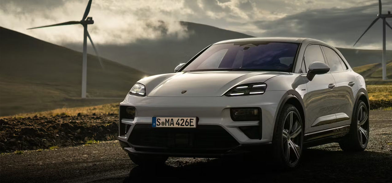 Vue 3/4 avant et latérale de la Porsche Macan EV 2024 sur route de terre avec éolienne