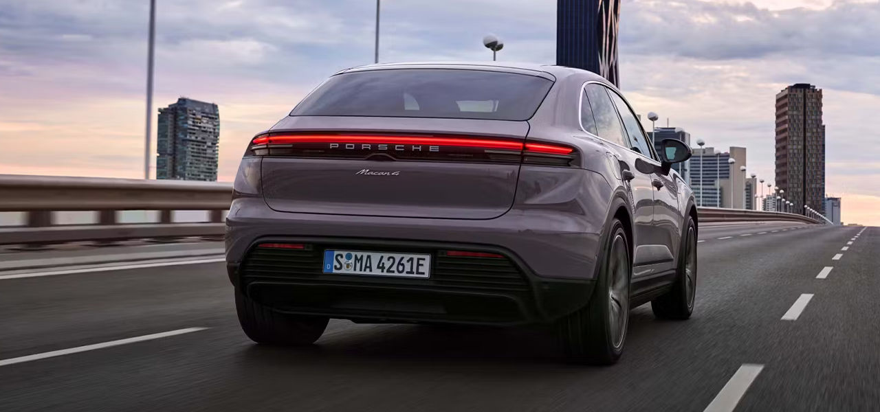 Vue arrière de la Porsche Macan EV 2024 sur route avec vue sur ville