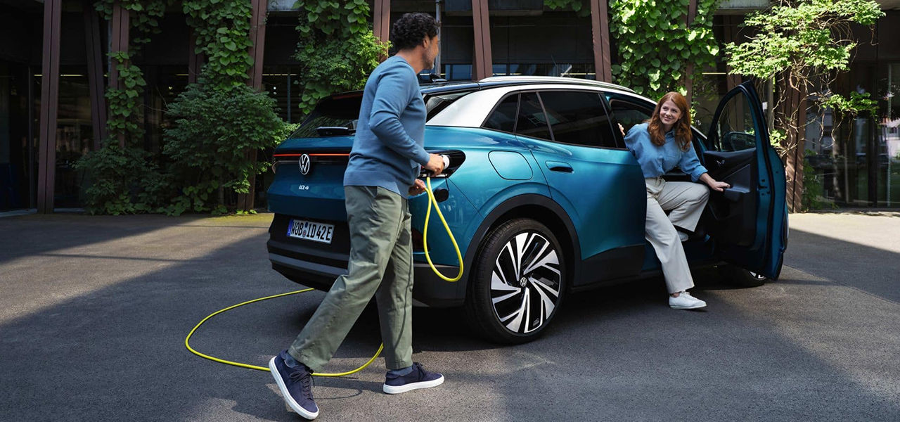 Vue d'une Vw ID.4 2024 avec une couple qui s'aprrêtent a recharger la voiture