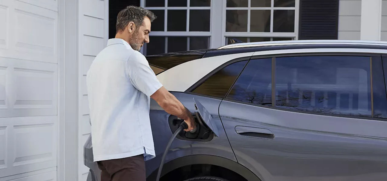 Vue latérale d'une VW ID.4 électrique avec une homme rechargeant la voiture avec une borne a domicile