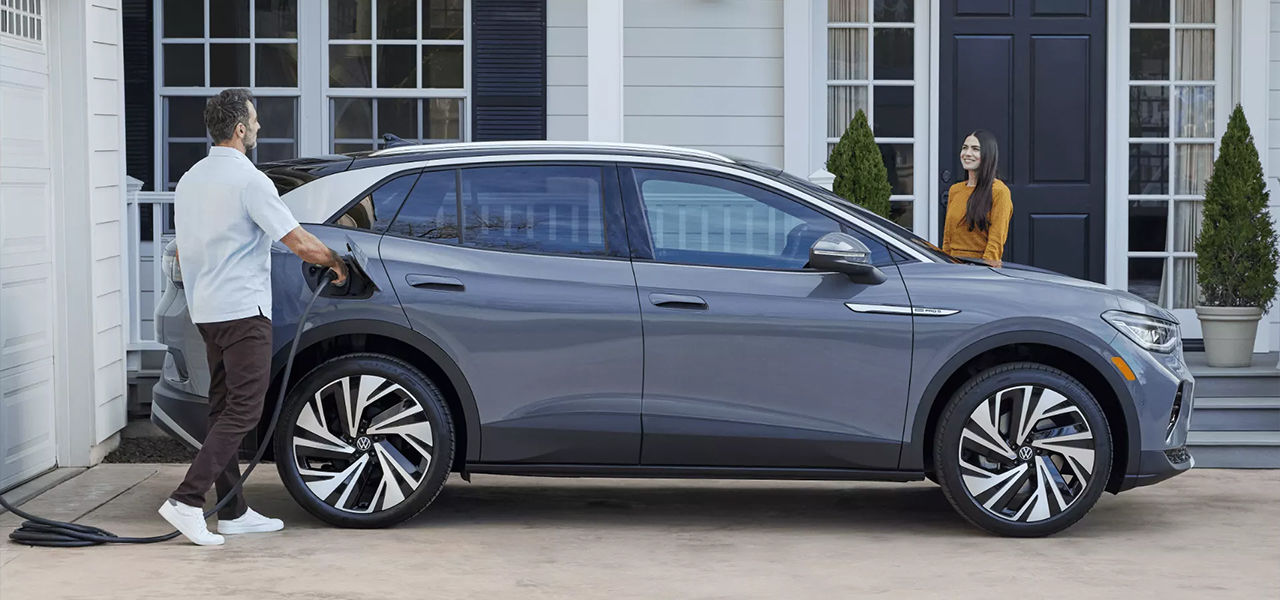 Side view of an electric VW ID.4 with a family charging the car with a home charging station