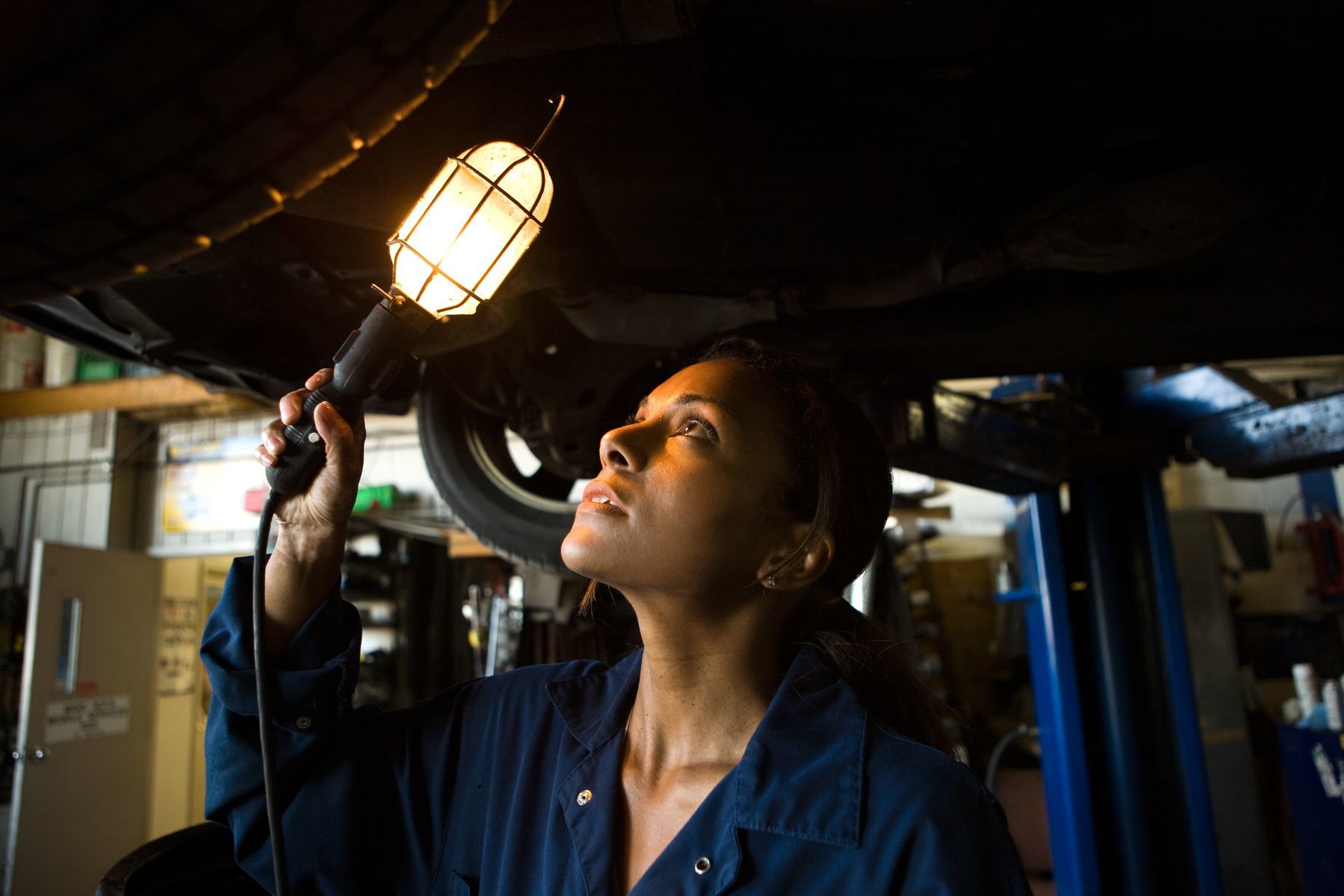 mécanicienne observant avec une lampe le dessous d'un véhicule en réparation