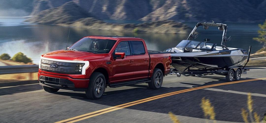 Vue 3/4 avant et latérale du Ford F-150 Lightning 2024 sur route avec remorque et bateau