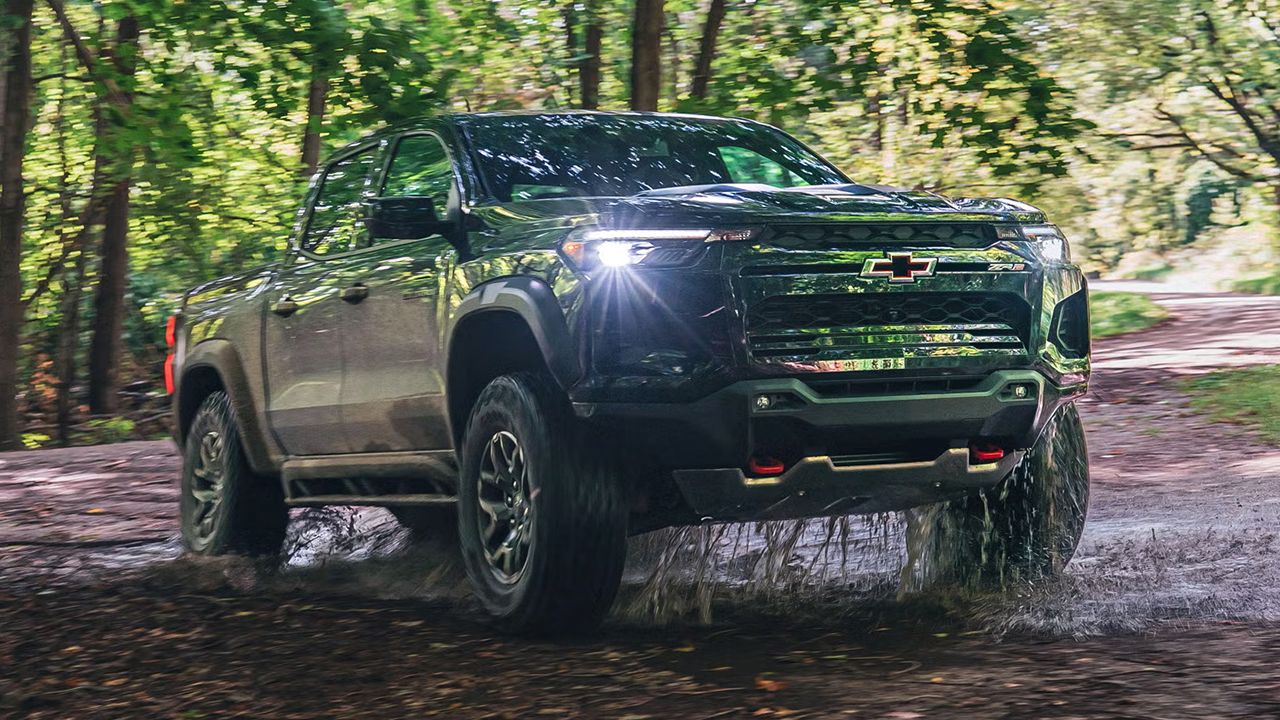 Vue 3/4 avant et lat&eacute;rale du Chevy Colorado 2026, sur chemin de for&ecirc;t, traversant une marre d'eau