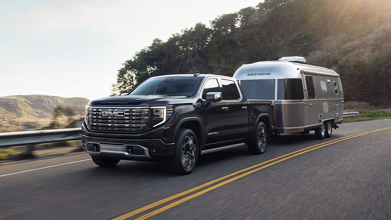 Vue avant et lat&eacute;rale du GMC Sierra 1500 2026 sur route tirant une remorque