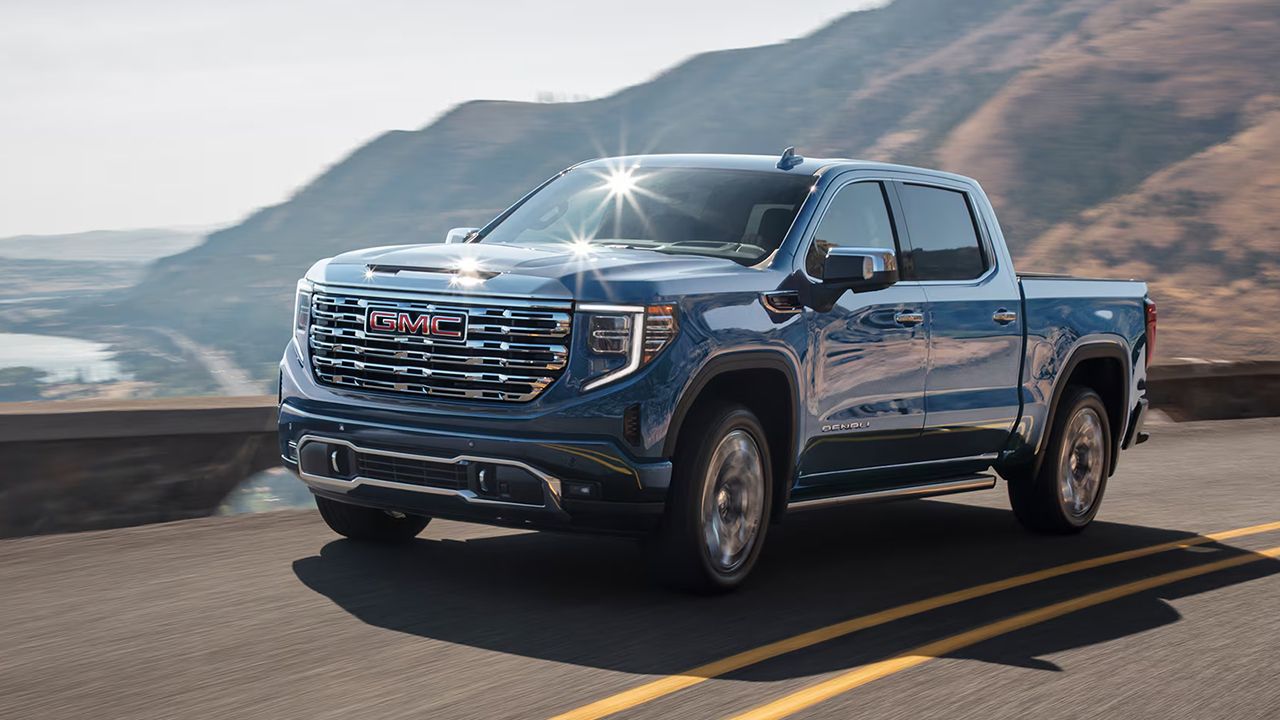 Vue avant et lat&eacute;rale du GMC Sierra 1500 2026 sur route, une journ&eacute;e ensoleil&eacute;