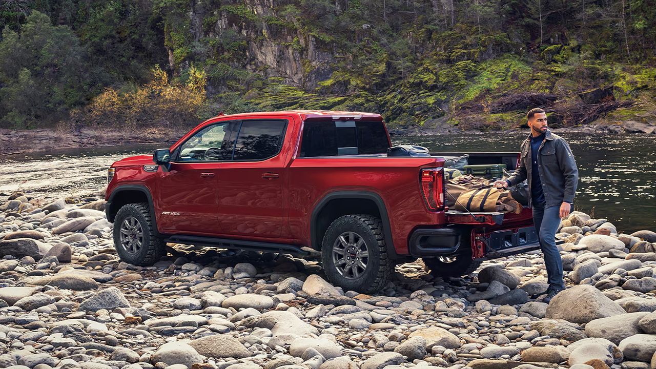 Vue arri&egrave;re du GMC Sierra 1500 2026 et d'un homme sortant un &eacute;quipement de camping et de p&ecirc;che