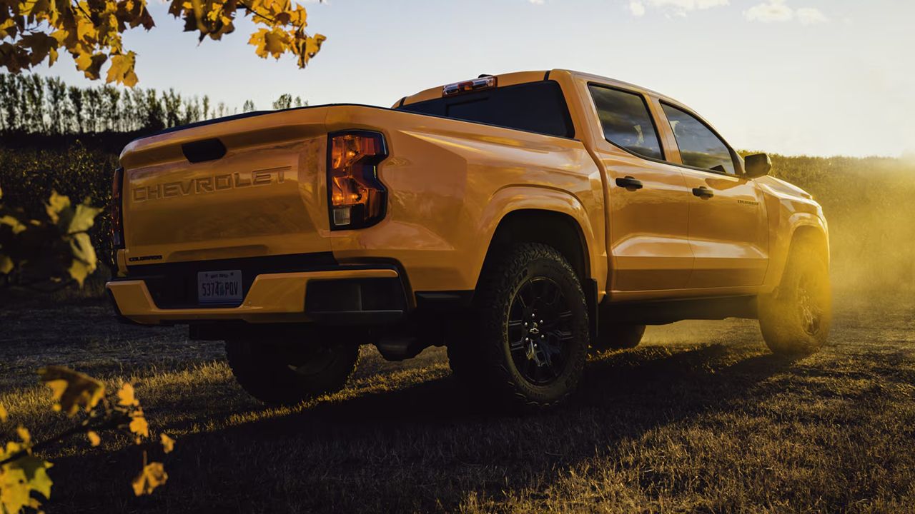 Vue arri&egrave;re du Chevrolet Colorado 2026 en arr&ecirc;t dans un champ avec un lever de soleil