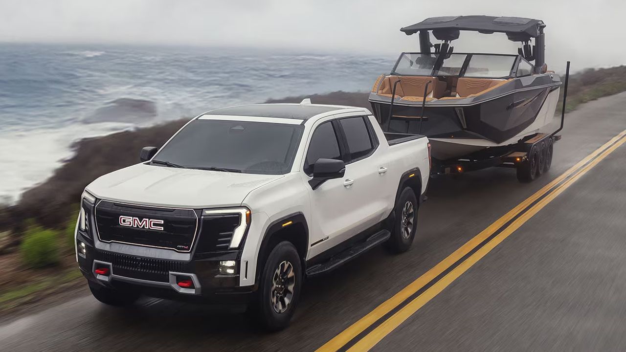 Vue 3/4 avant et lat&eacute;rale du GMC Sierra EV 2026 sur route tirant un bateau
