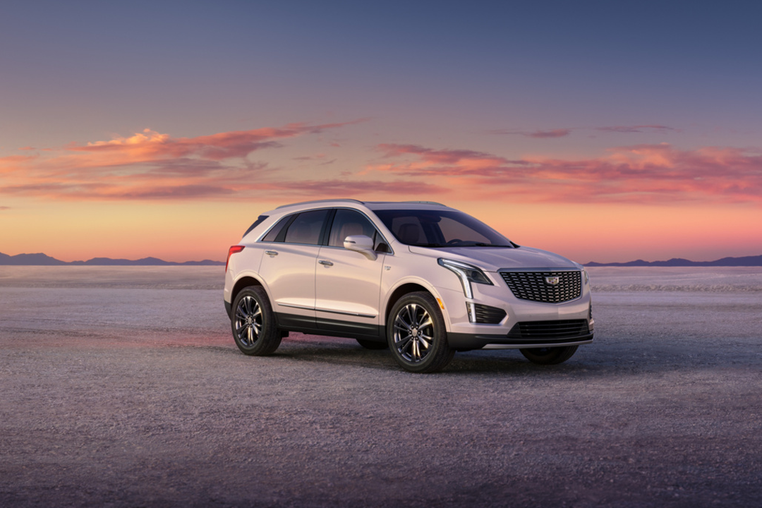 Front and side view of the Cadillac XT5 2024 on a sandy road with sunset.