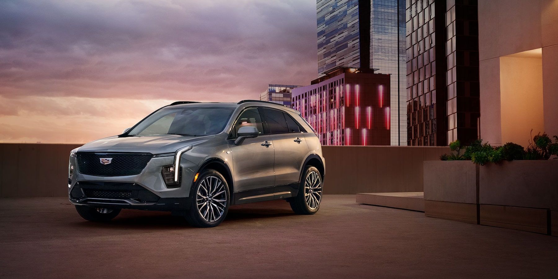 Cadillac XT4 2025 vu de face devant une résidence avec des gratte-ciels en arrière plan pendant un coucher de soleil