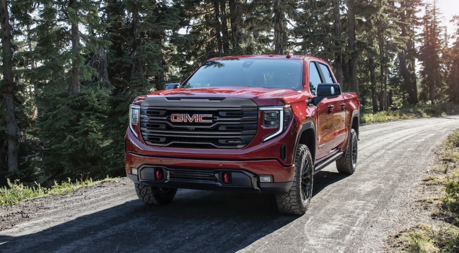 red 2022 at4 gmc sierra pickup truck driving on a tree lined road near montreal