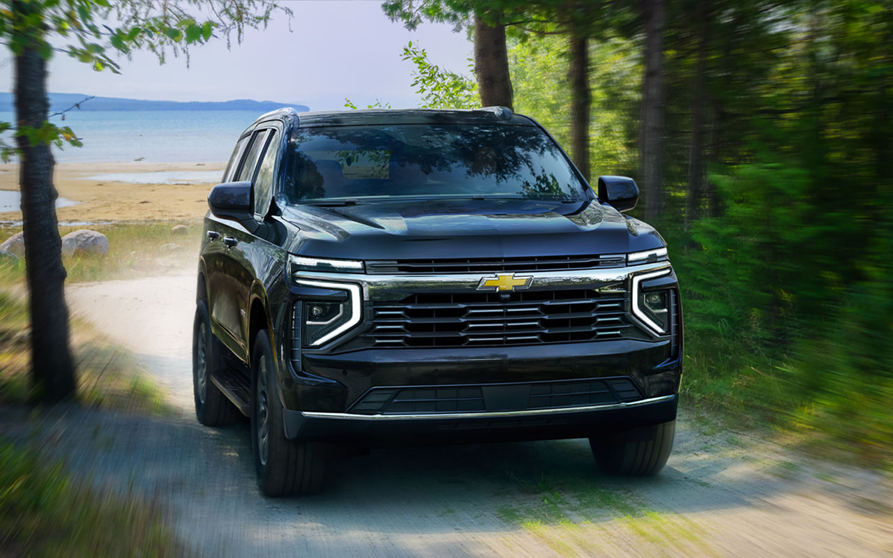 Vue 3/4 avant et latérale du Chevrolet Suburban 2025 sur route de sable et vue sur mer