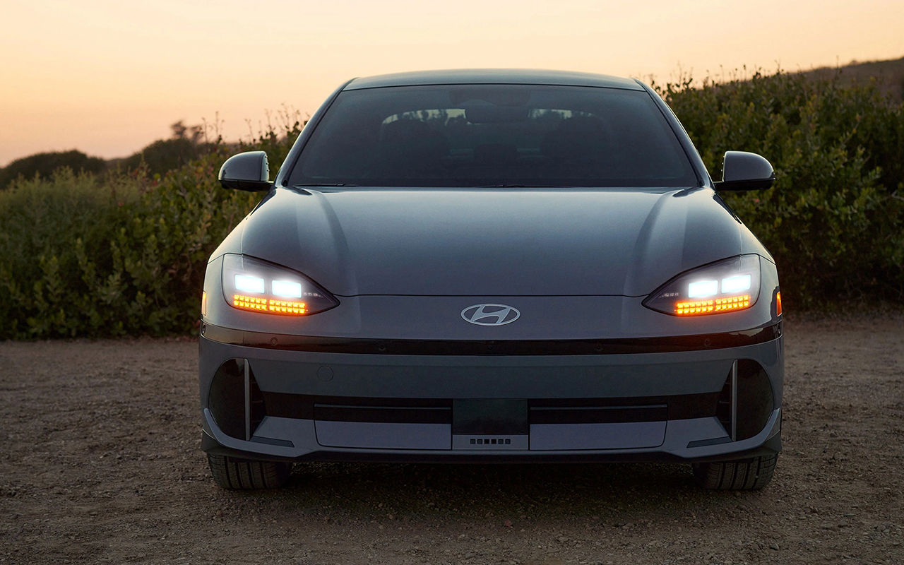 Vue avant de la Hyundai IONIQ 6 2025 sur le sable avec phares allumée et coucher de soleil