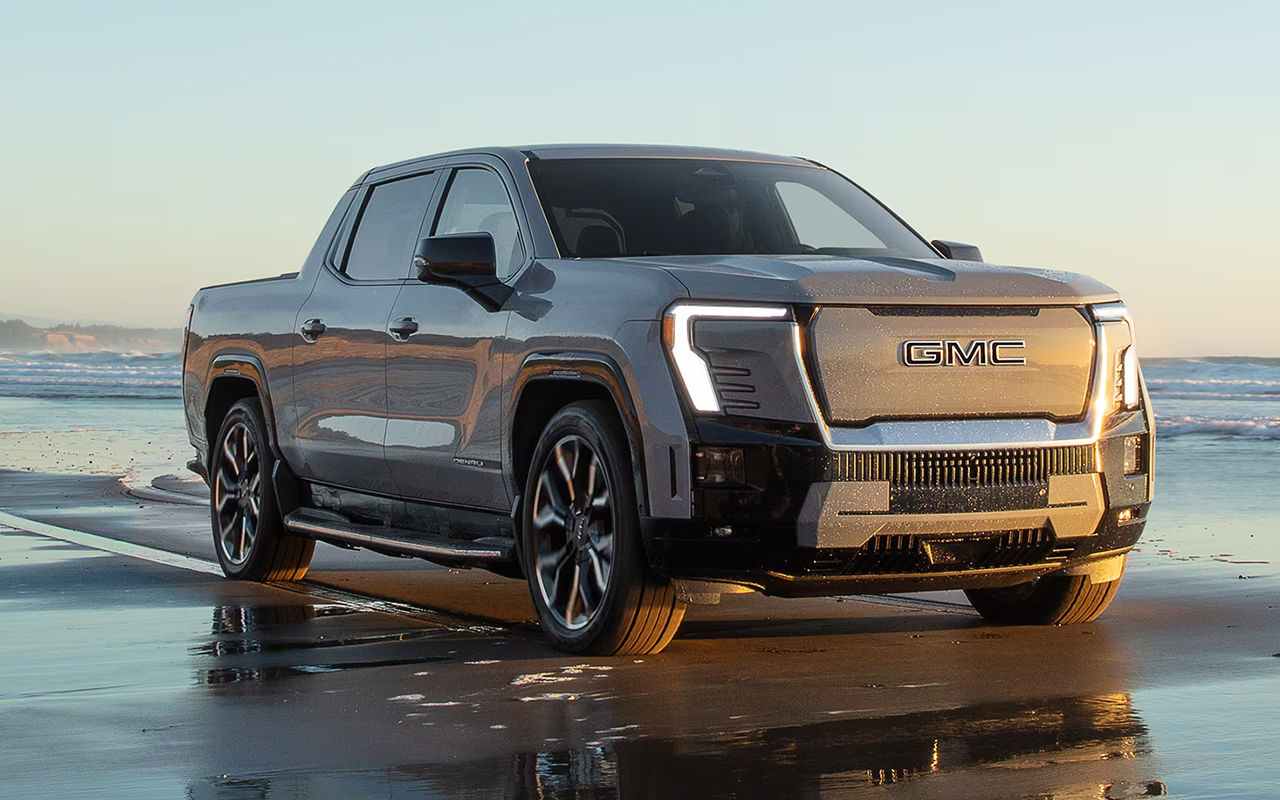 Vue 3/4 avant et latérale du Sierra EV Denali sur plage et mer au coucher de soleil