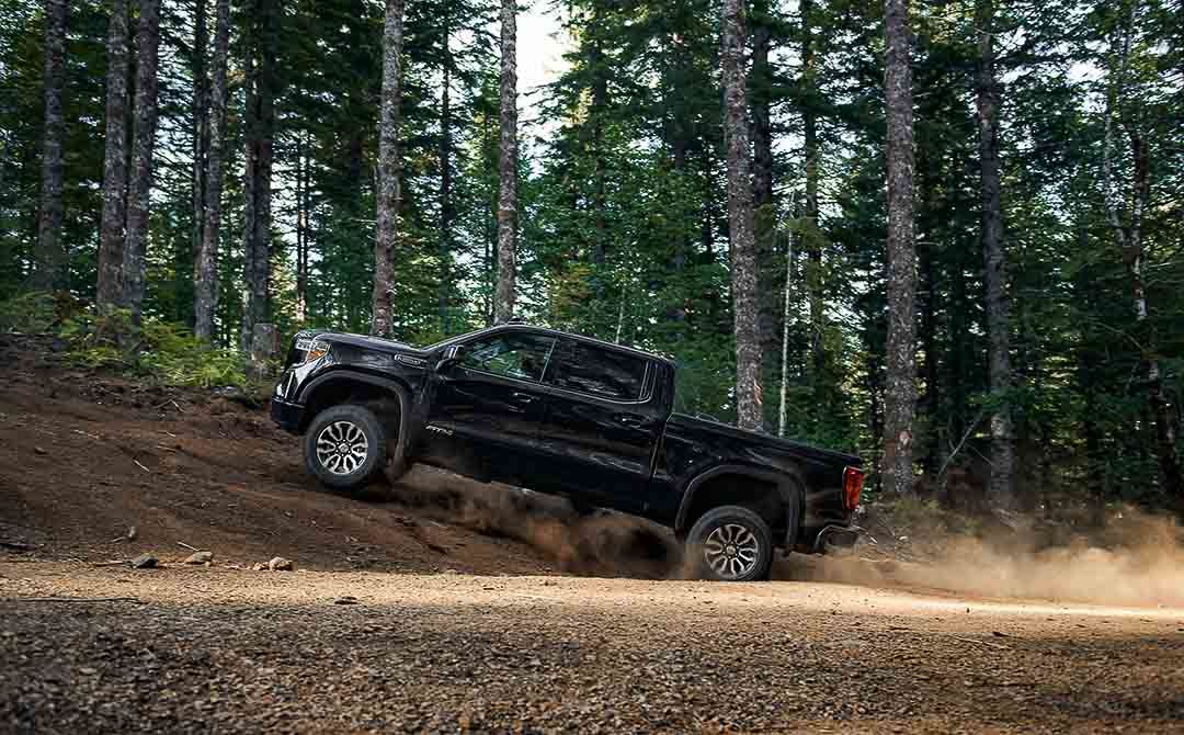 vue latérale du GMC Sierra 1500 AT4 2021 sur en terrain en forêt