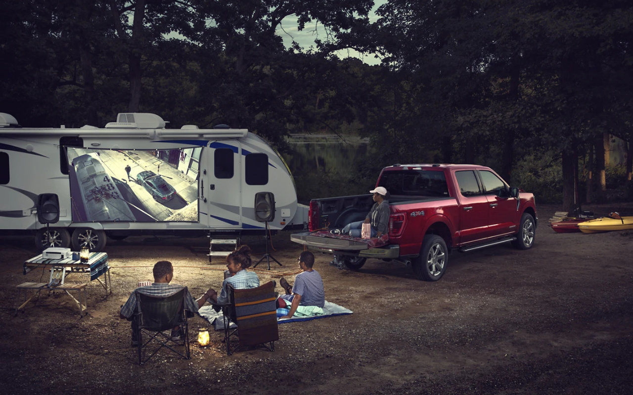 vue d'une famille qui écoute un film en camping à côté d'un camion Ford F-150 2023 et une maison remorque