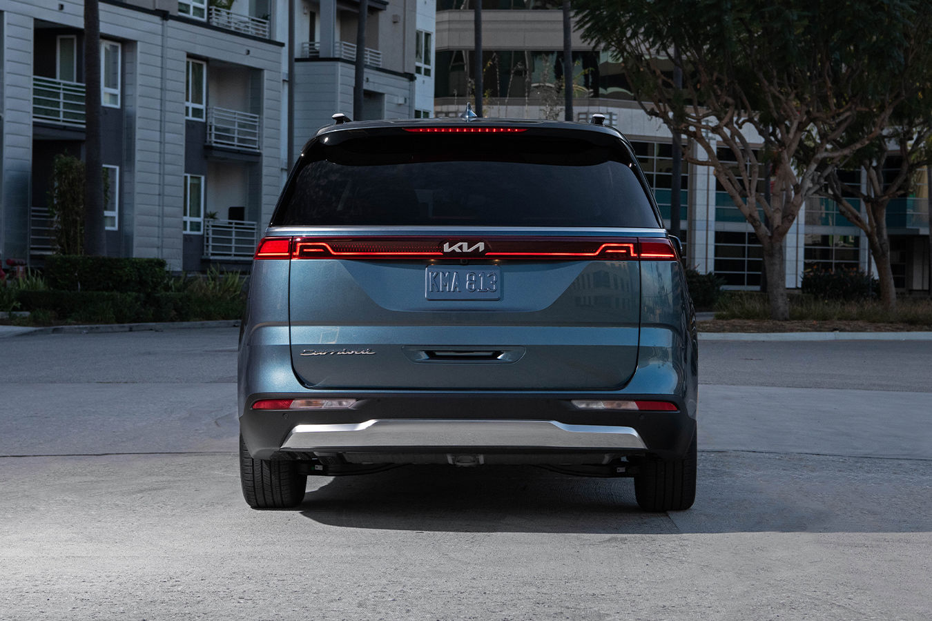 Rear view of the Kia Carnival 2025 in a parking lot in front of a building