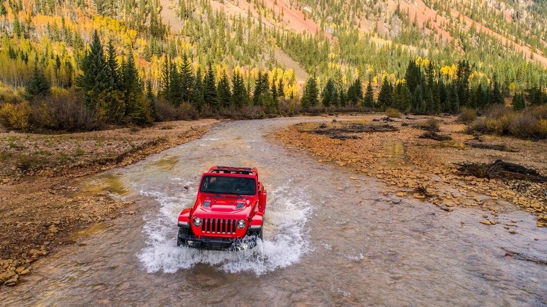 vue frontale éloignée d'un Jeep Wrangler 2023 dans un cours d'eau en montagne