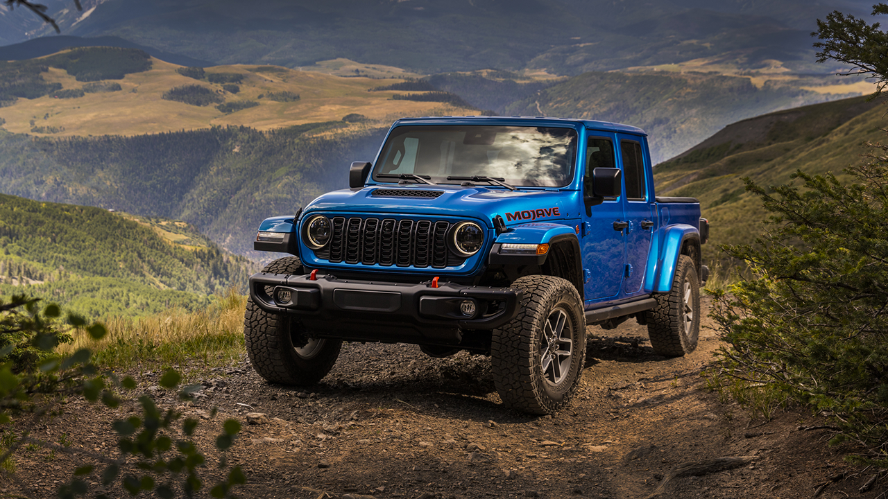 Vue 3/4 avant et latérale du Jeep Gladiator, en arrêt sur chemin de montagne avec vue sur collines