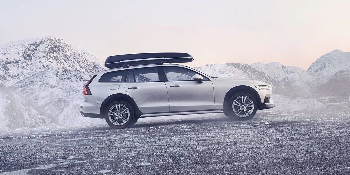 Volvo with roof box, winter car accessories, snowy mountains, Volvo side profile.