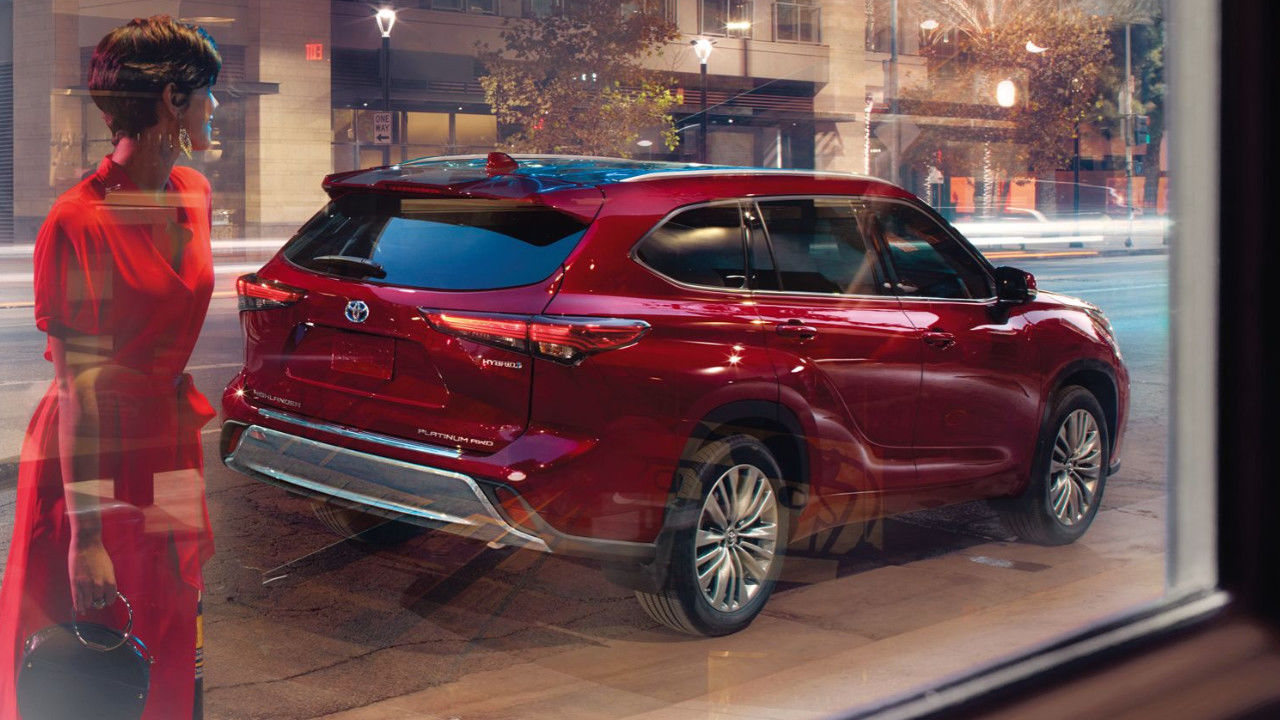 rear side view of a 2023 Toyota Highlander in front of a boutique with a women in an elegant red dress