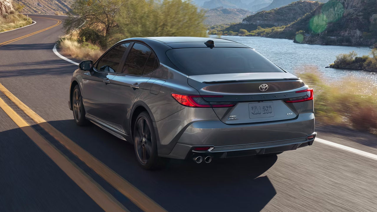 Rear view of the Toyota Camry hybrid 2025, on the road at full power with river view