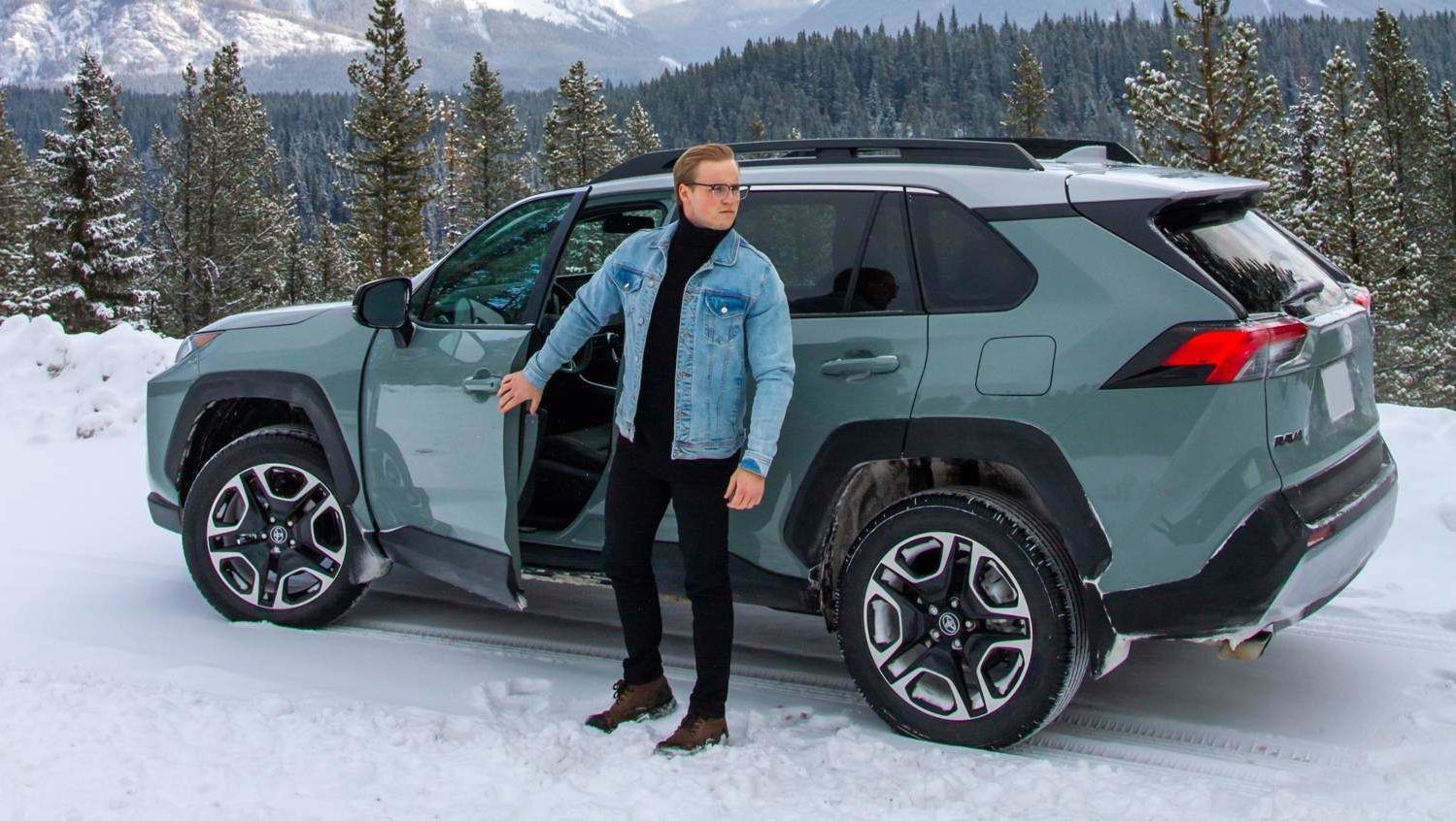 man stepping out of gray 2021 Toyota RAV4 SUV to look outside in forest during winter season