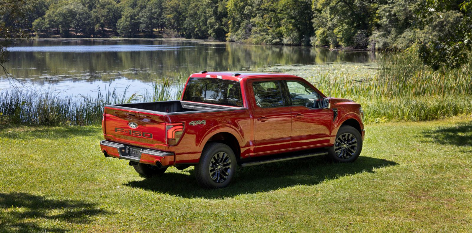 2025 Ford F-150 - rear three-quarter view of a red 2025 Ford F-150 Lariat parked on grass by a lake - Bayfield Ford - Ford car dealership in Barrie, ON