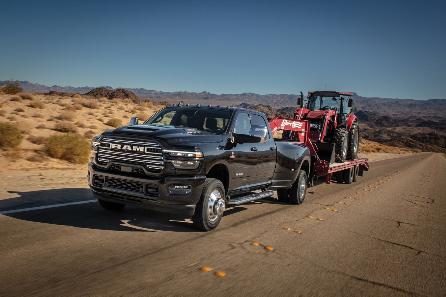 2025 Ram 3500 a black dually truck towing a tractor on a flatbed trailer - Cooksville Dodge - Ram car dealership in Mississauga, Ontario