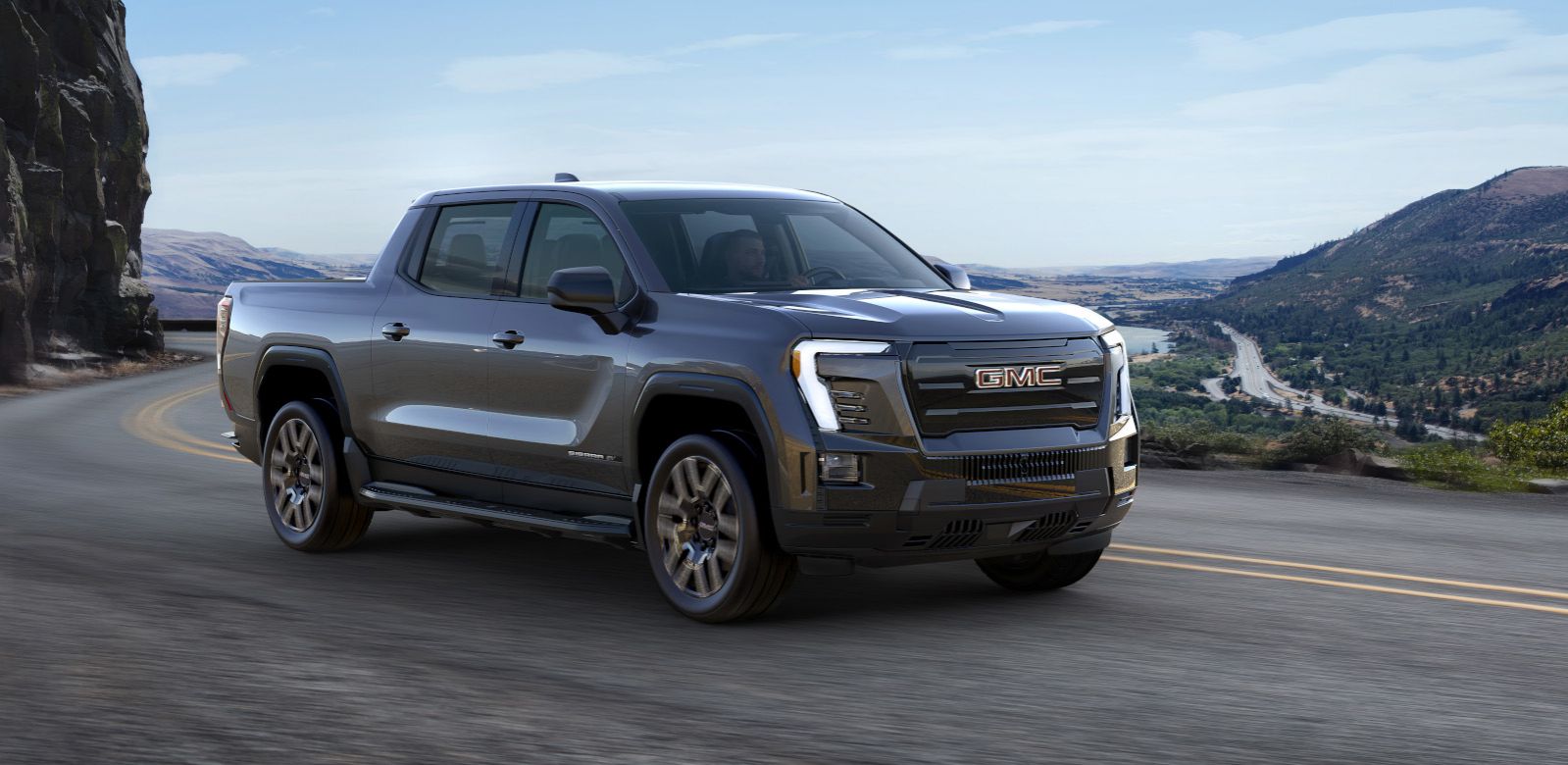 2026 GMC Sierra EV - a dark gray 2026 GMC Sierra EV driving on a winding road - Humberview Chevrolet - GMC car dealership in Toronto, Ontario