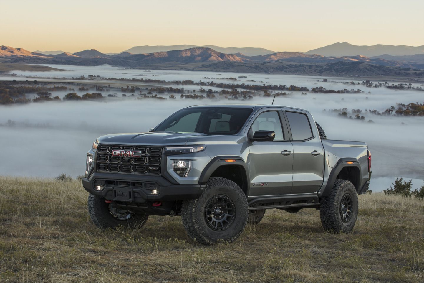 2025 GMC Canyon AT4X AEV - a silver 2025 GMC Canyon AT4X AEV parked on a grassy hill overlooking a foggy valley - Applewood Chevrolet Buick GMC - GMC car dealership in Mississauga, Ontario