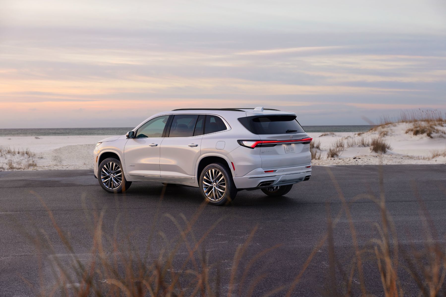 2025 Buick Enclave - a white 2025 Buick Enclave Avenir parked on a road next to a sandy beach at dusk - Humberview Chevrolet Buick GMC - Buick car dealership in Toronto, Ontario