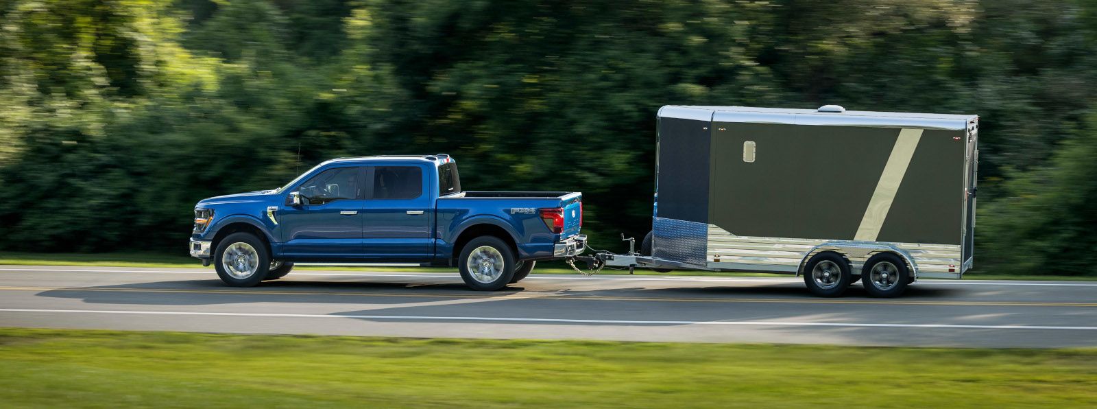 2025 Ford F-150 - a blue XLT trim shown from the side while towing a black enclosed trailer - Mayfield Ford - new car dealerships in Ontario