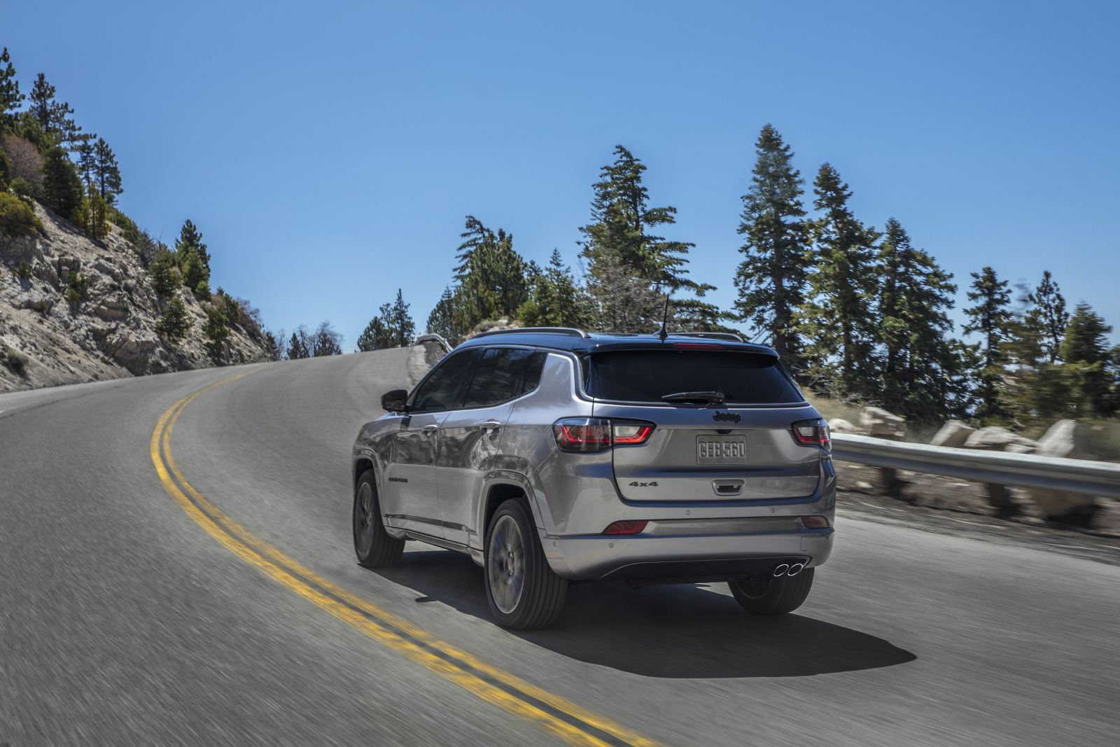 2025 Jeep Compass a silver 2025 Jeep Compass driving on a paved, winding road through a forest - Cooksville Dodge - new car dealerships in Ontario