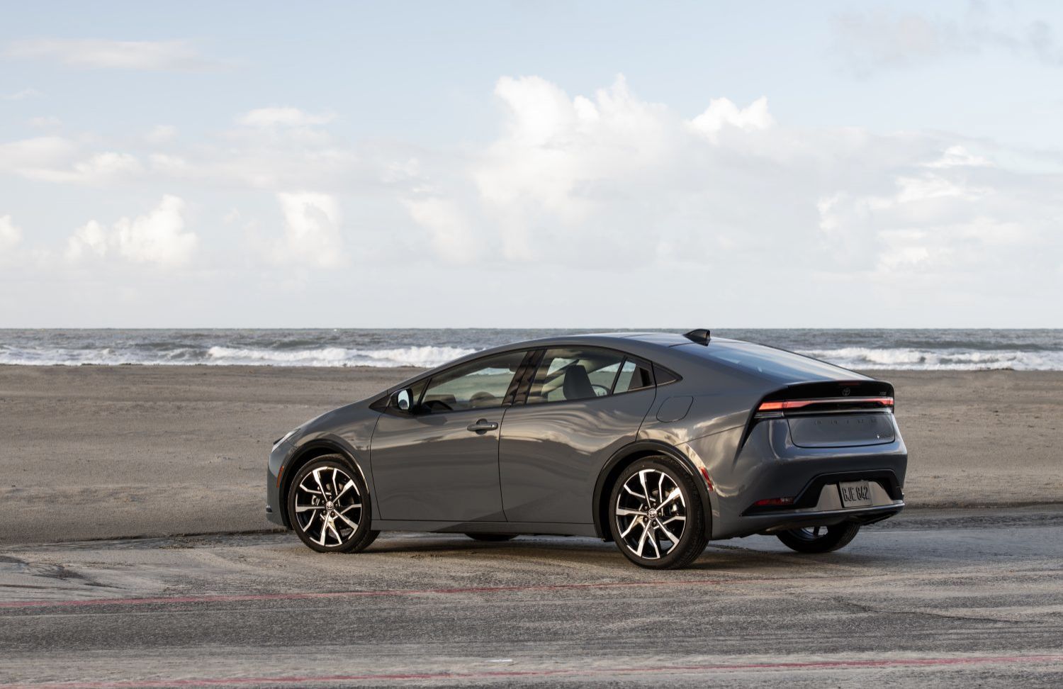 2025 Toyota Prius Prime - a gray 2025 Toyota Prius Prime parked on a beach with the ocean in the background - Oakville Toyota - Toyota car dealership in Oakville, Ontario